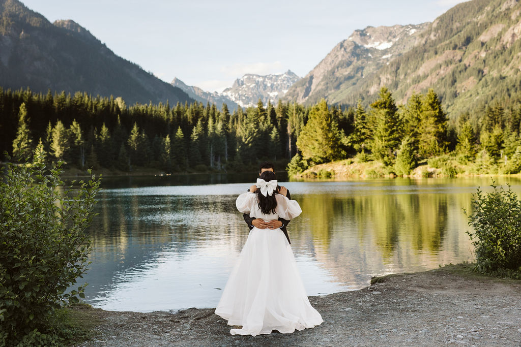 bride and groom stand in front of lake hugging