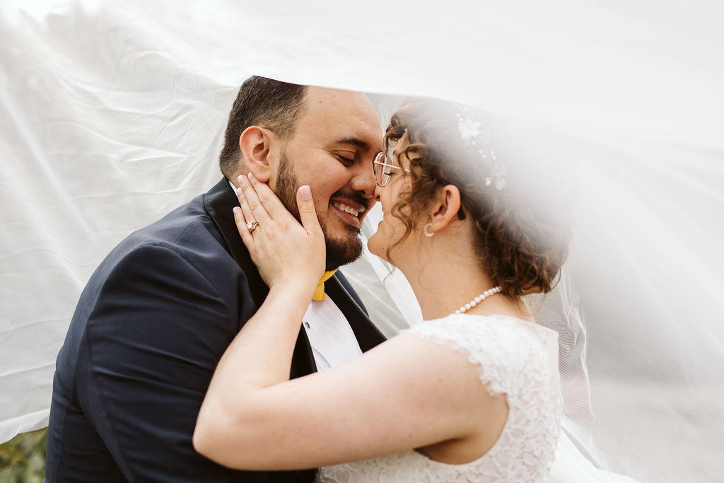 bride and groom snuggle under veil and smile at each other