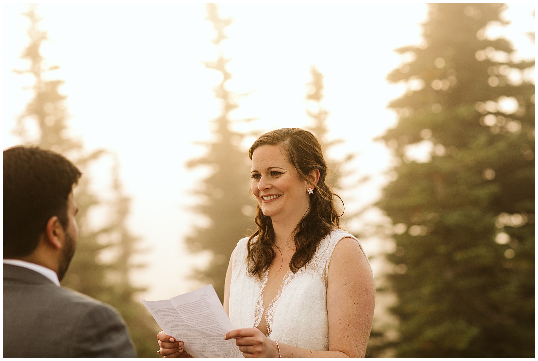 emily holds her printed vows, smiling at jay during their elopement ceremony in mount rainier.