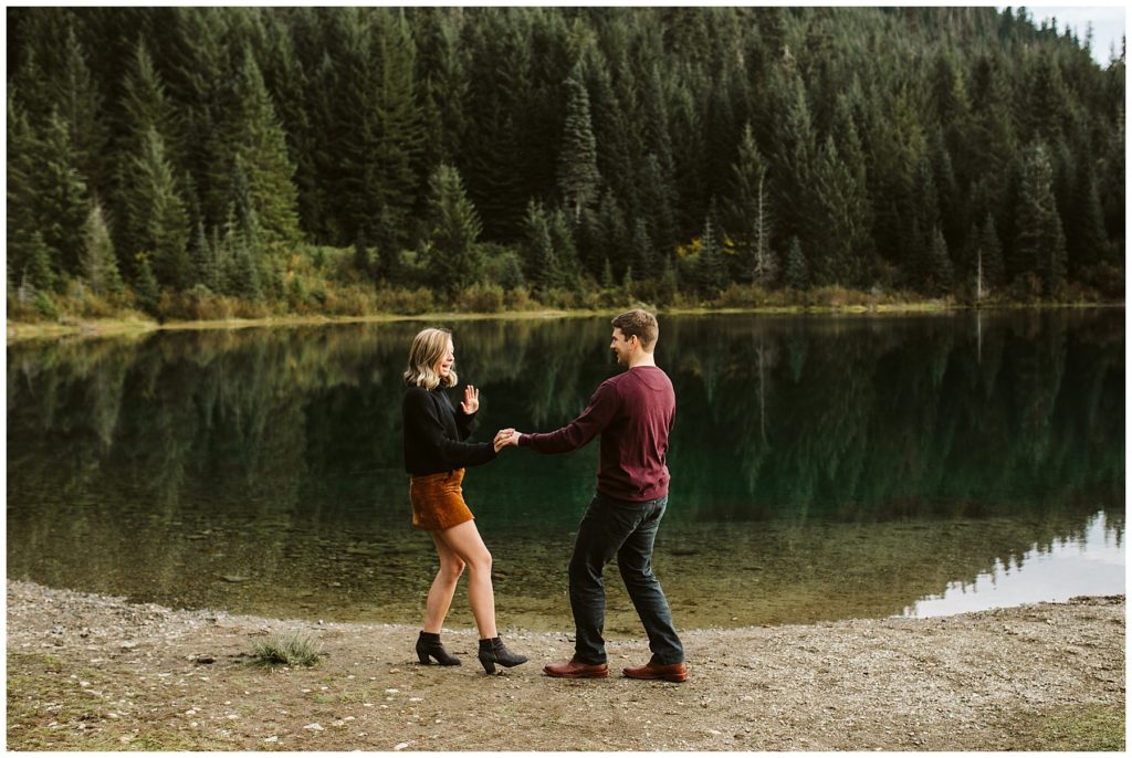 couple dancing and laughing fall engagement outfits lake with trees reflecting 