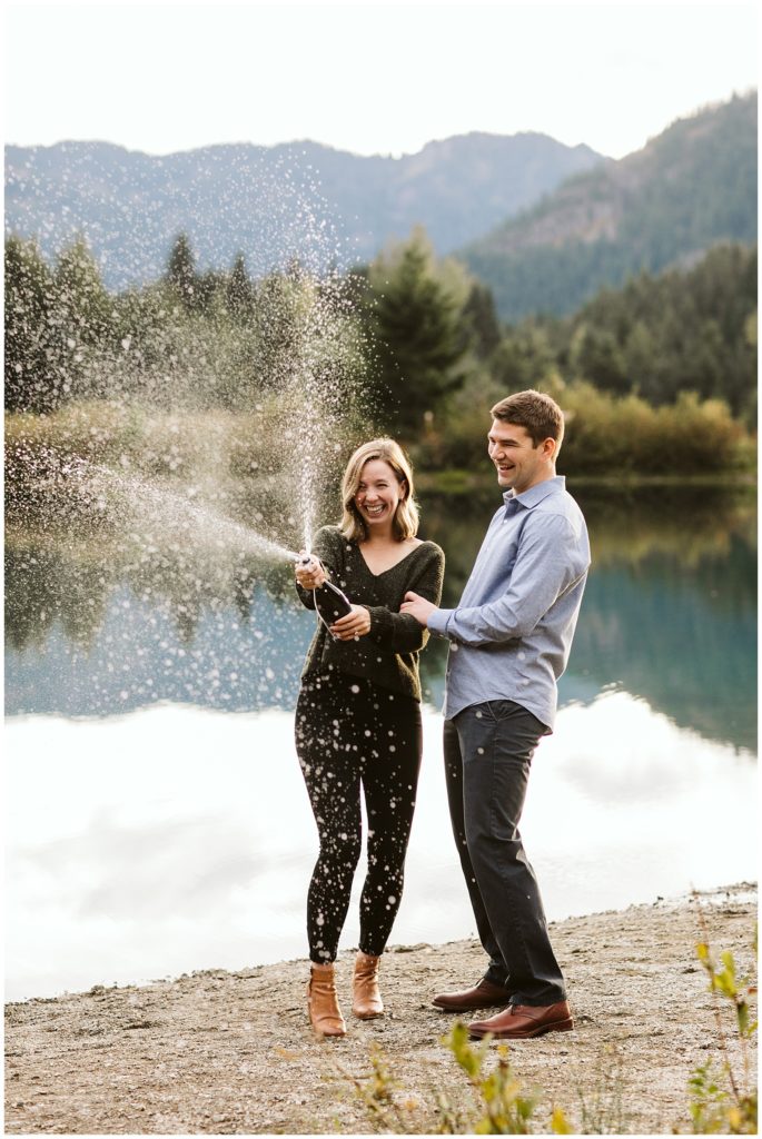 couple popping champagne lake and mountains in the background