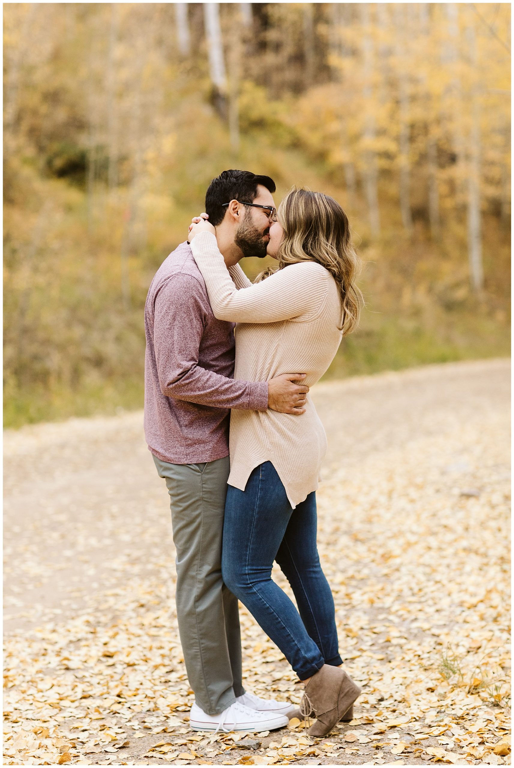 Couple kissing in road with aspen tree forest in background, a beautiful fall engagement photos backdrop.