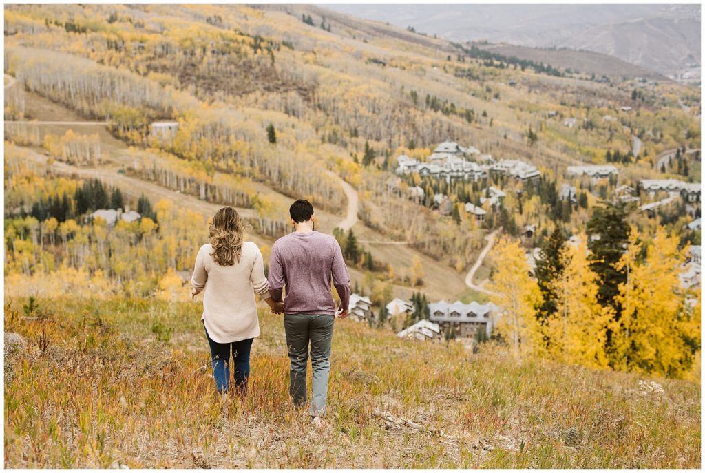 couple holding hands and walking into fall grassy field 