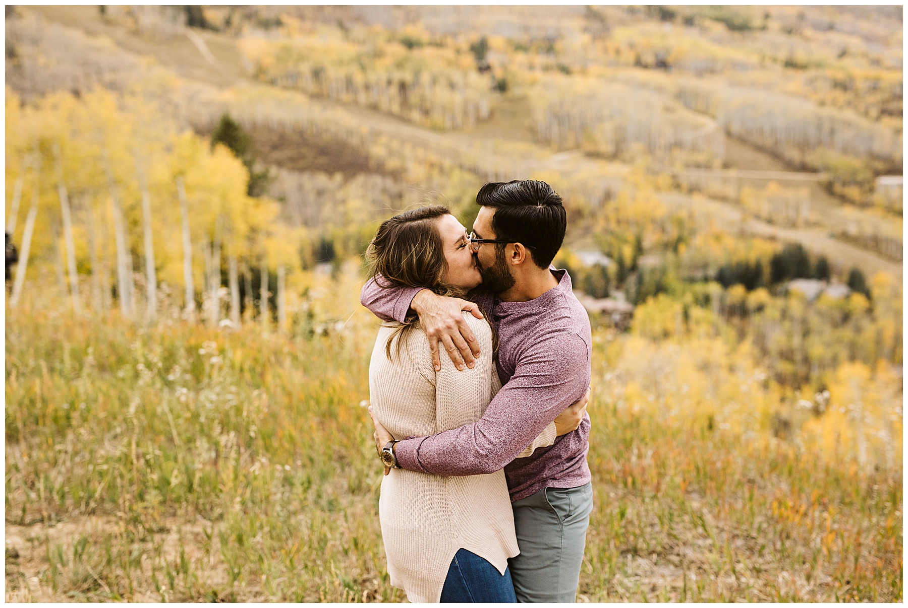couple kissing and hugging in yellow grassy field at their fall engagement photos session