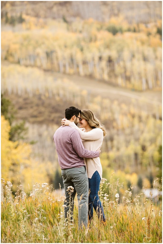 couple standing and touching foreheads in grassy field with fall colors in background