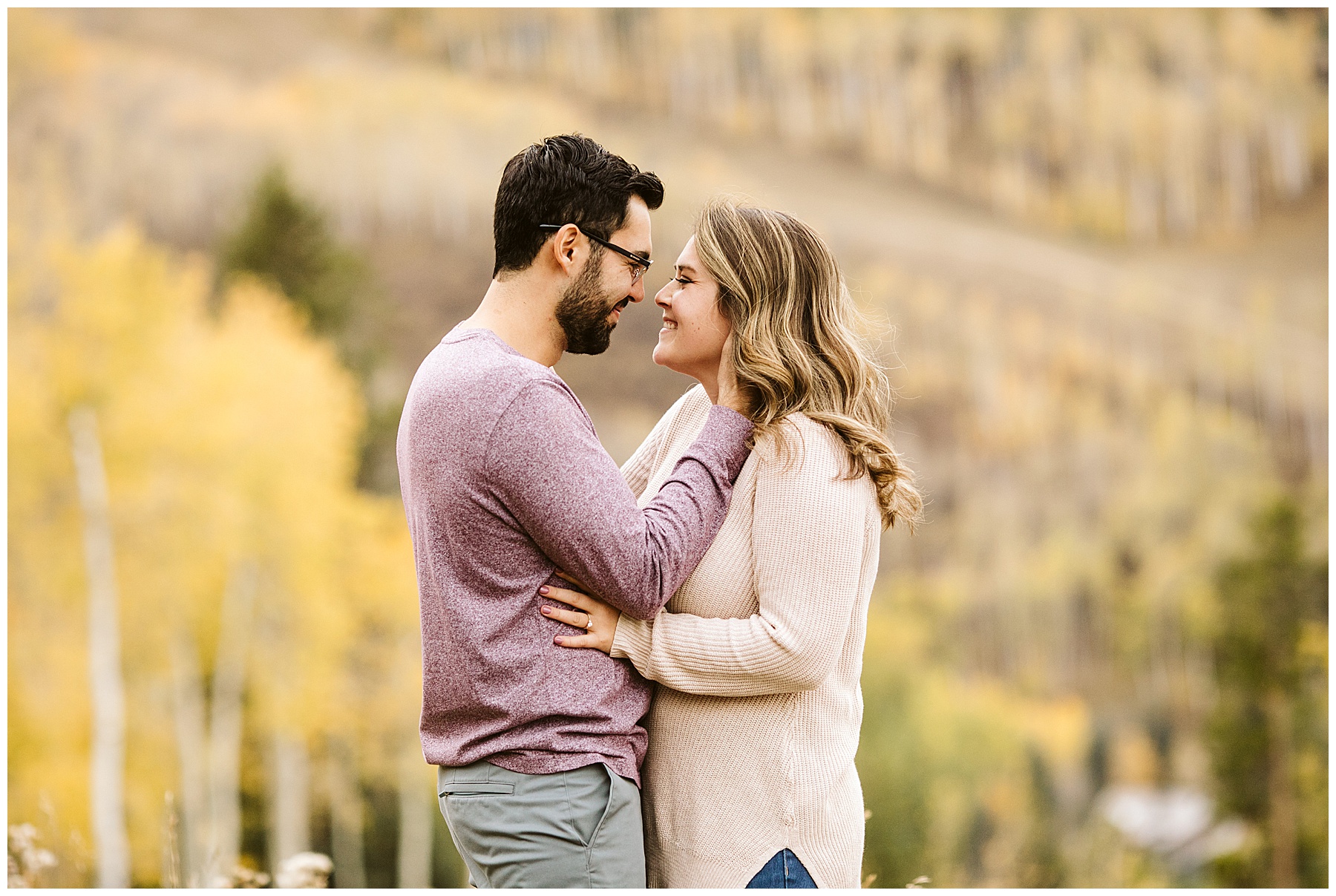 man holding woman close yellow trees in background at their fall engagement photos session