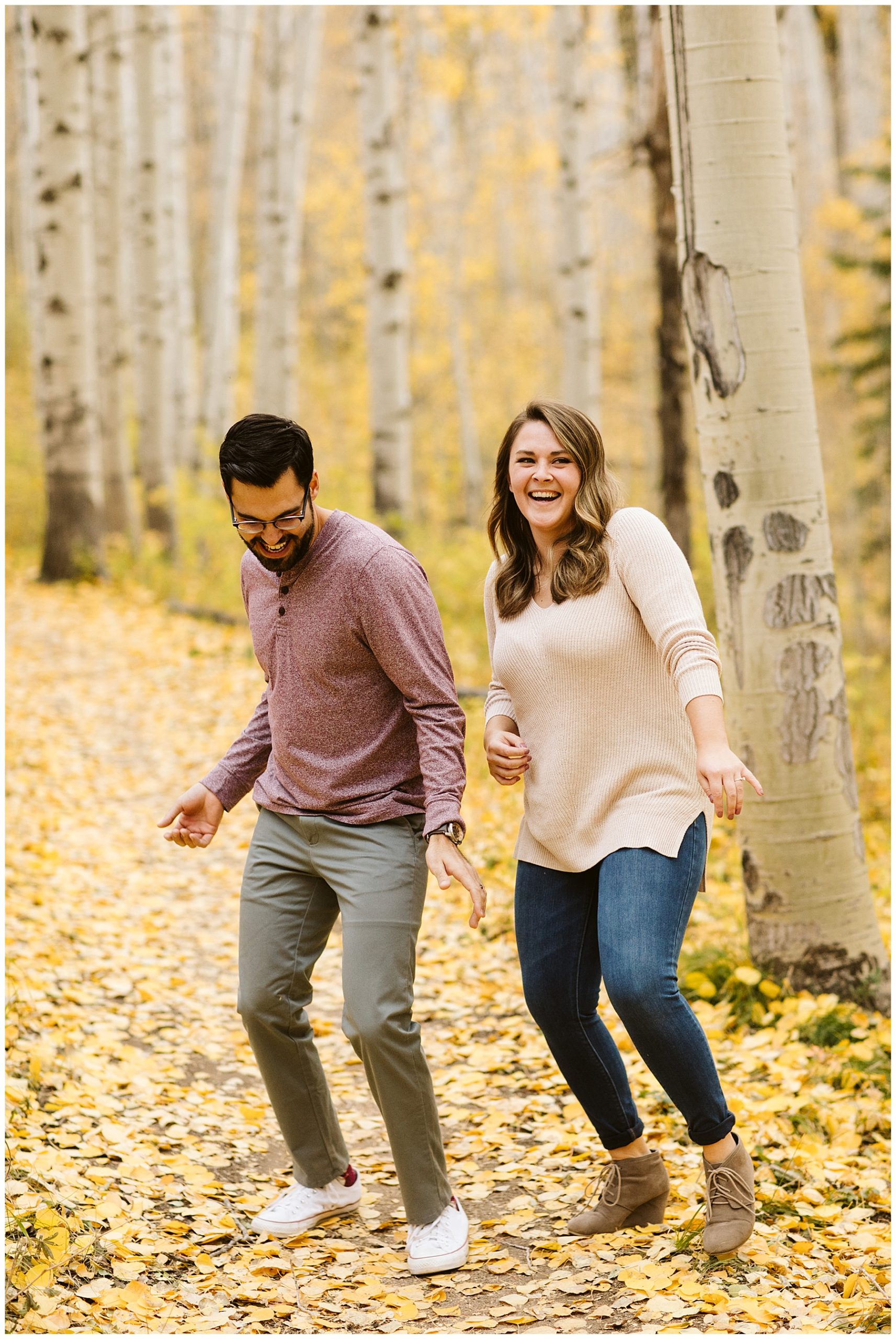 couple laughing in yellow aspen forest woman wearing cream sweater and jeans