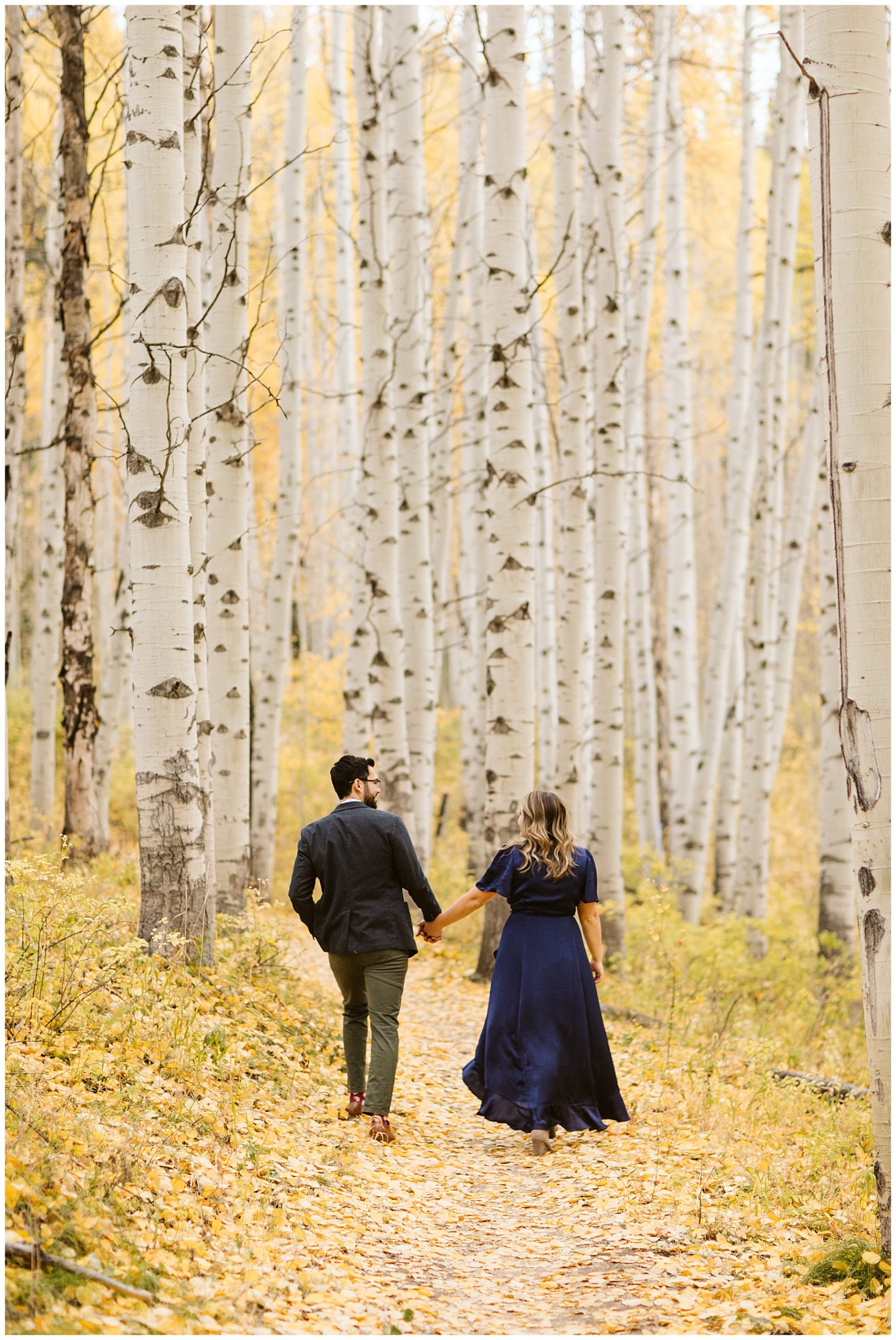 couple walking into yellow aspen forest in a navy blue dress and grey  suit