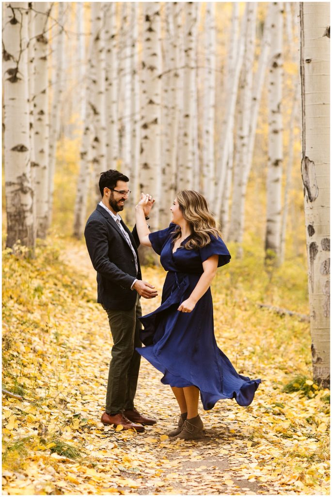 couple dancing in yellow aspen forest. blue dress flying in air