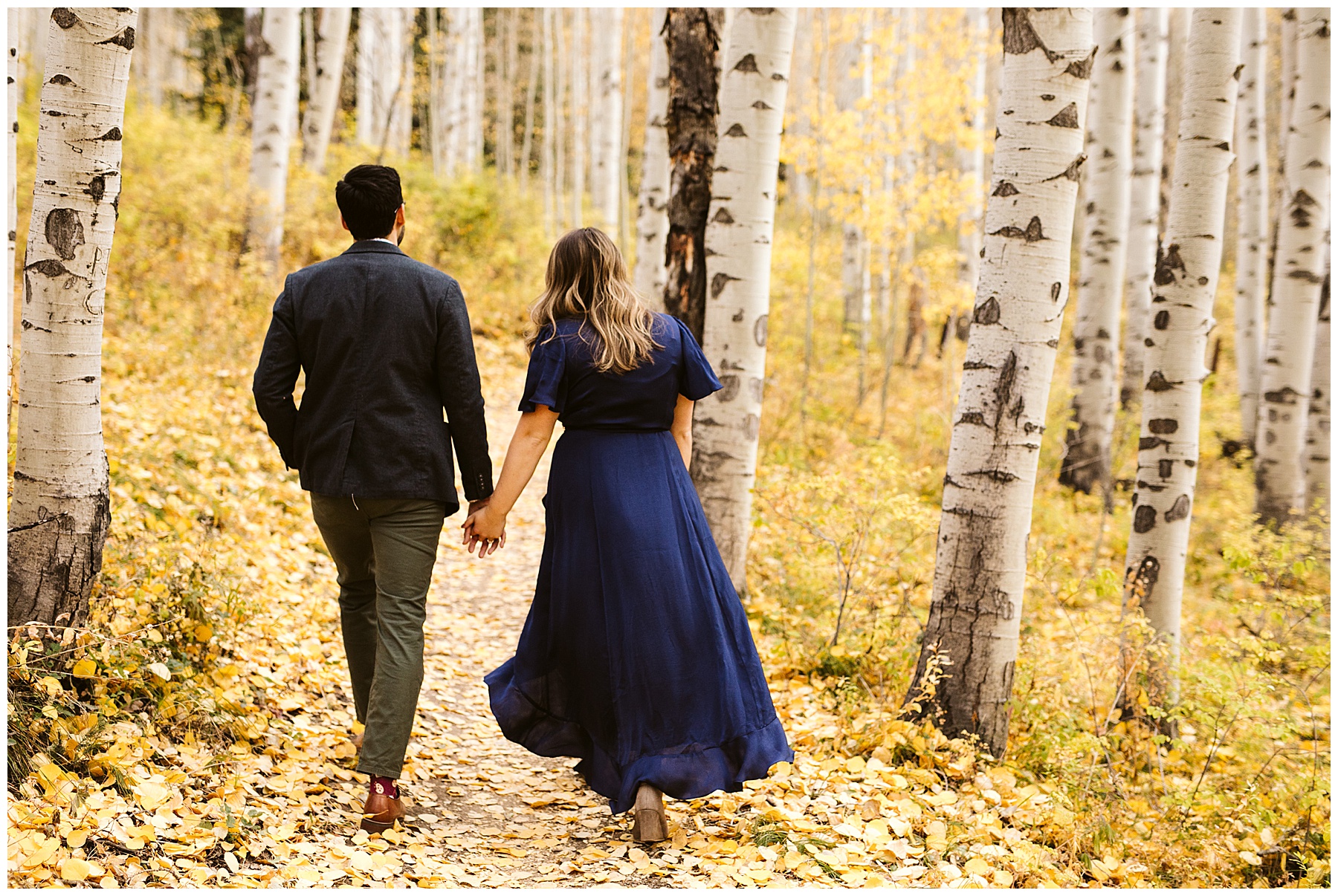 couple walking through aspen forest with blue dress; these fall engagement photos were taken in Colorado.