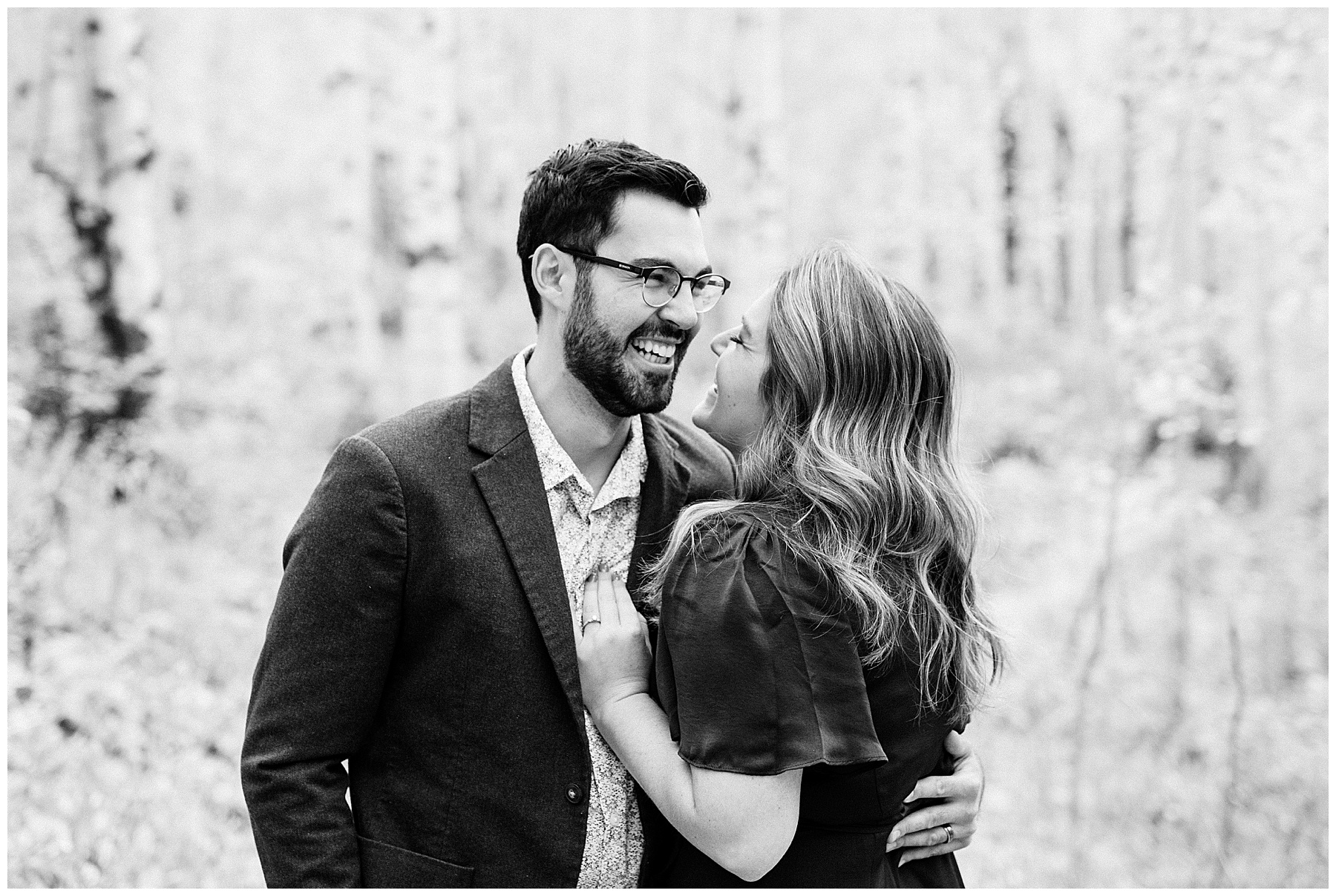 couple laughing in forest black and white fall engagement photo