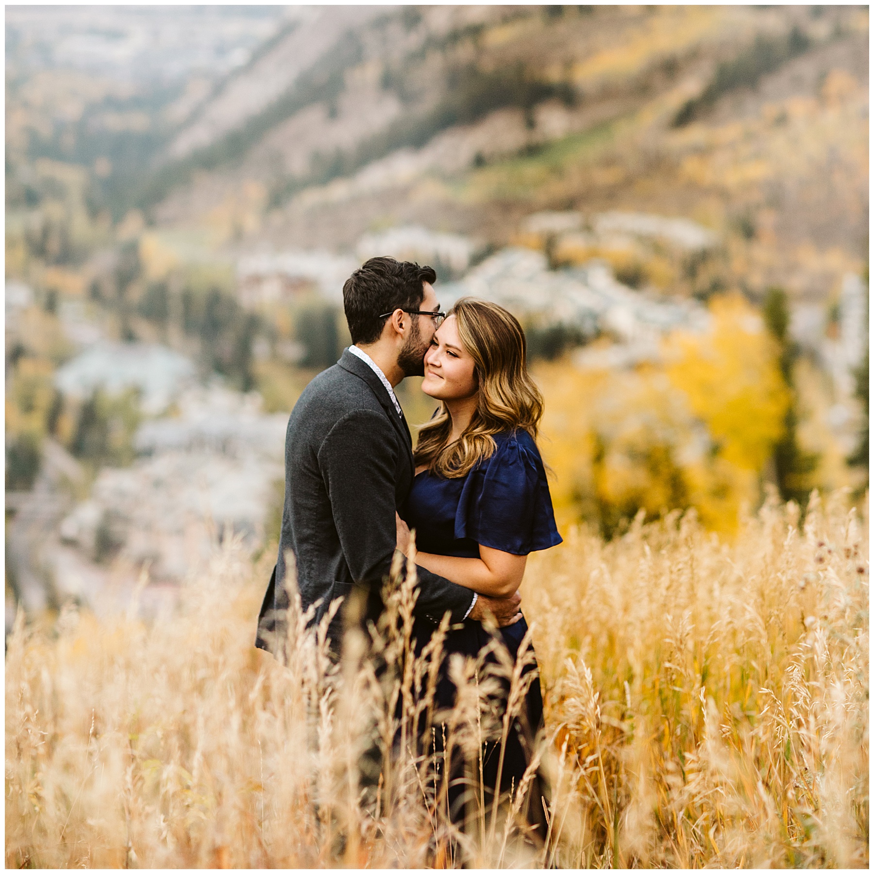man kissing woman on cheek with yellow aspen trees in the background; these fall engagement photos were taken in Colorado.