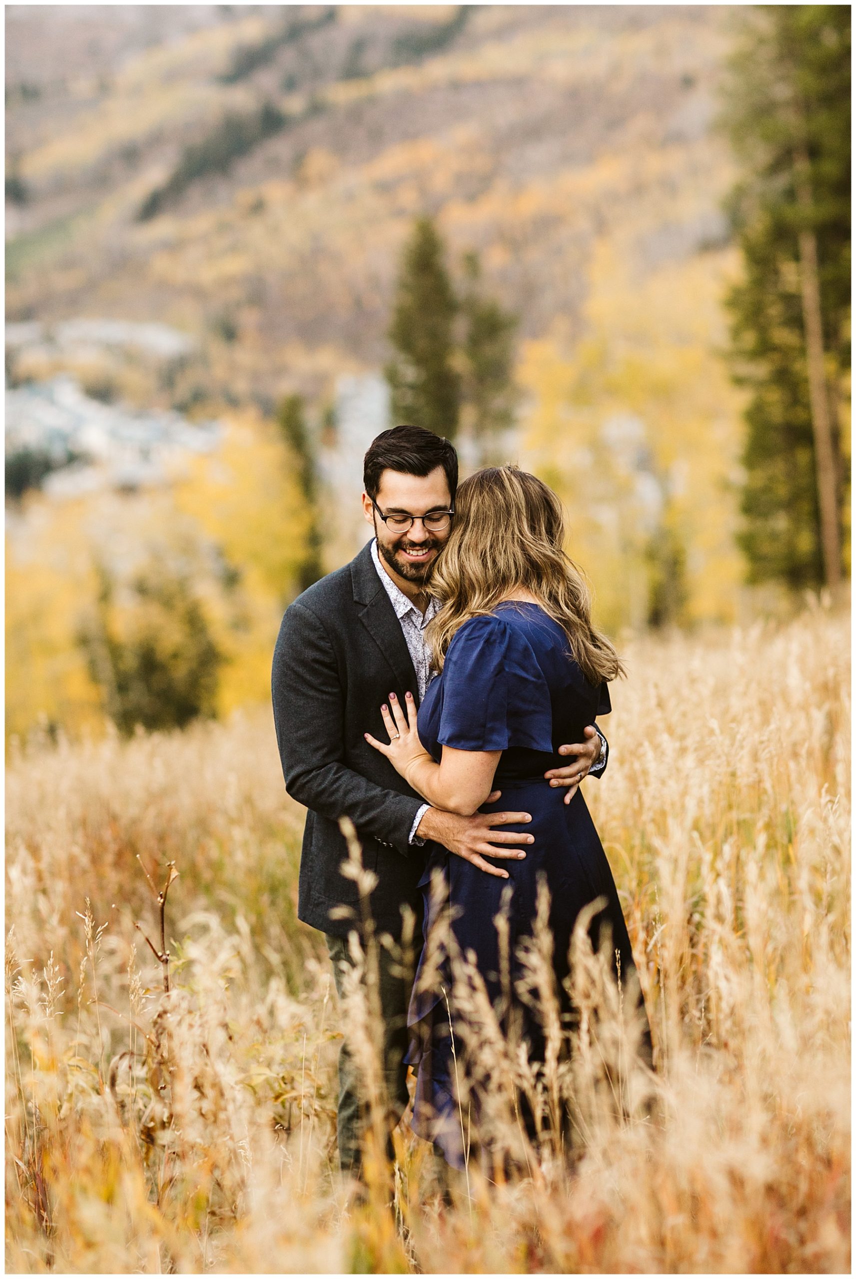 couple hugging in brown grassy field yellow trees in the background
