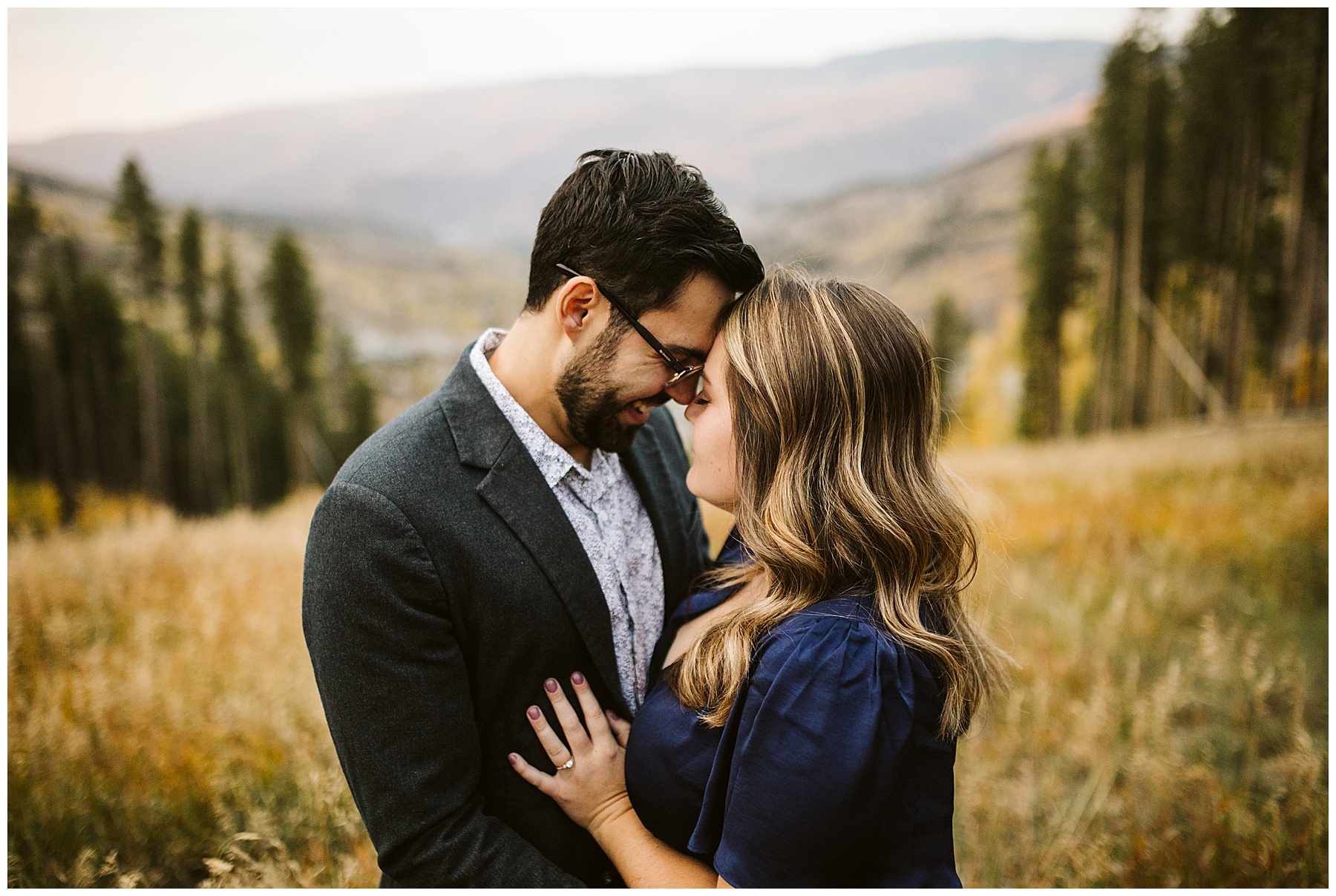 couple touching foreheads fall colors background; these fall engagement photos were taken in Colorado.