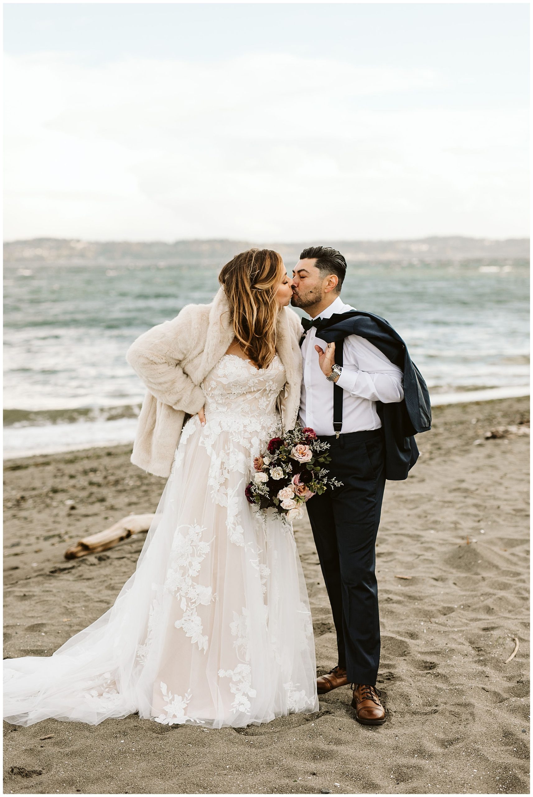 bride and groom kissing on the beach with water in the background