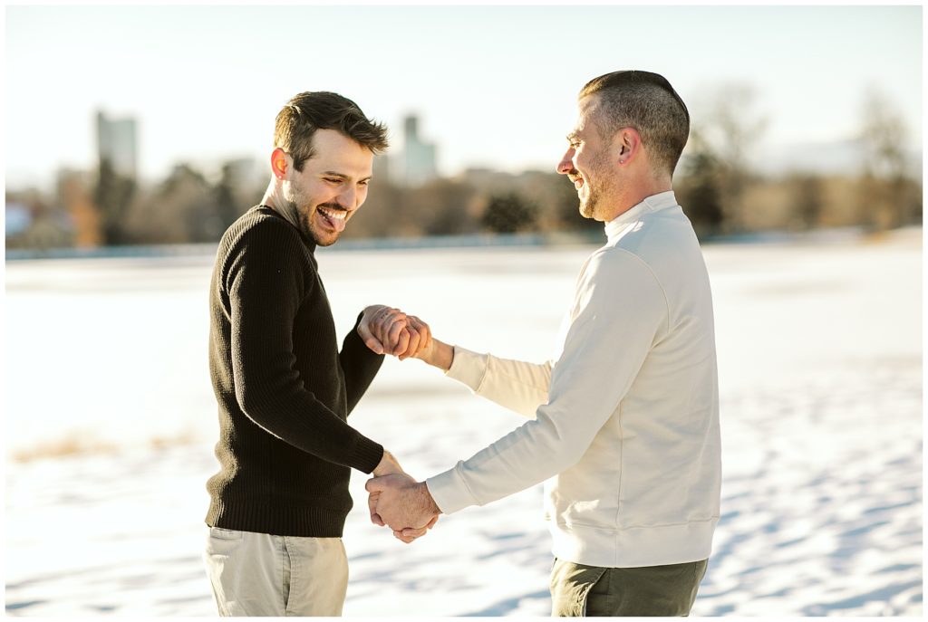 two men romantically holding hands and playing in the snow while smiling and laughing