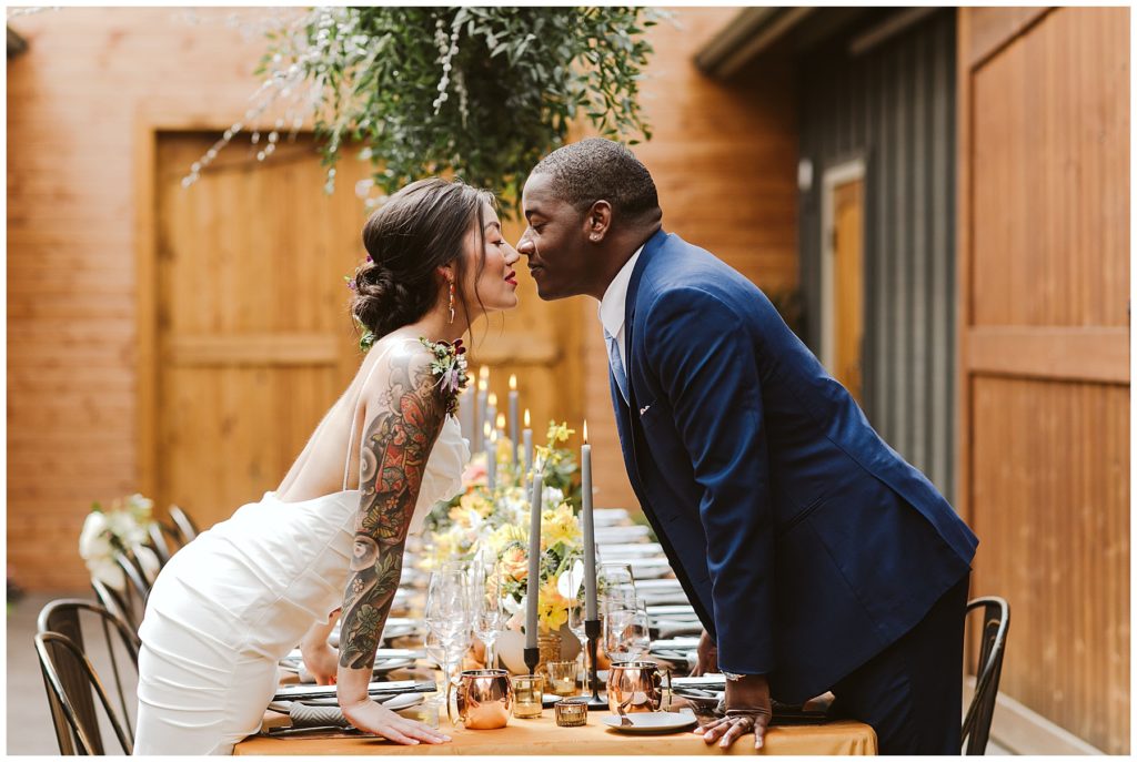 asian bride and black groom kissing over the long table with orange table cloth