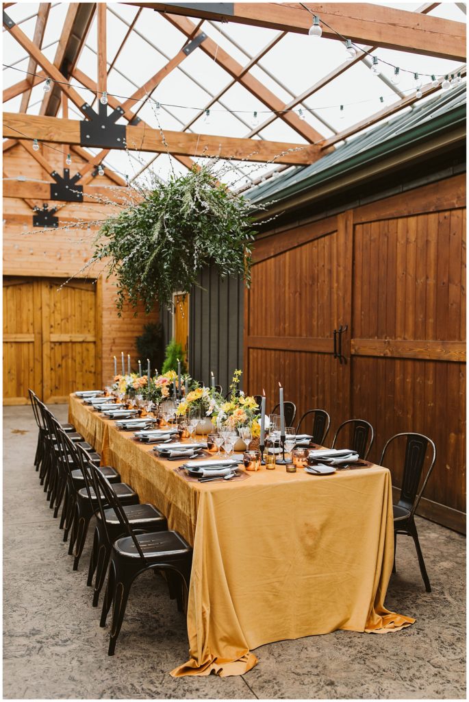 large green hanging plant chandelier over a long table with places set on an orange table cloth