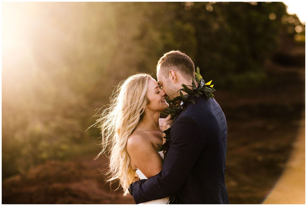blonde woman kissing a man with a  necklace of leaves around his neck at sunset