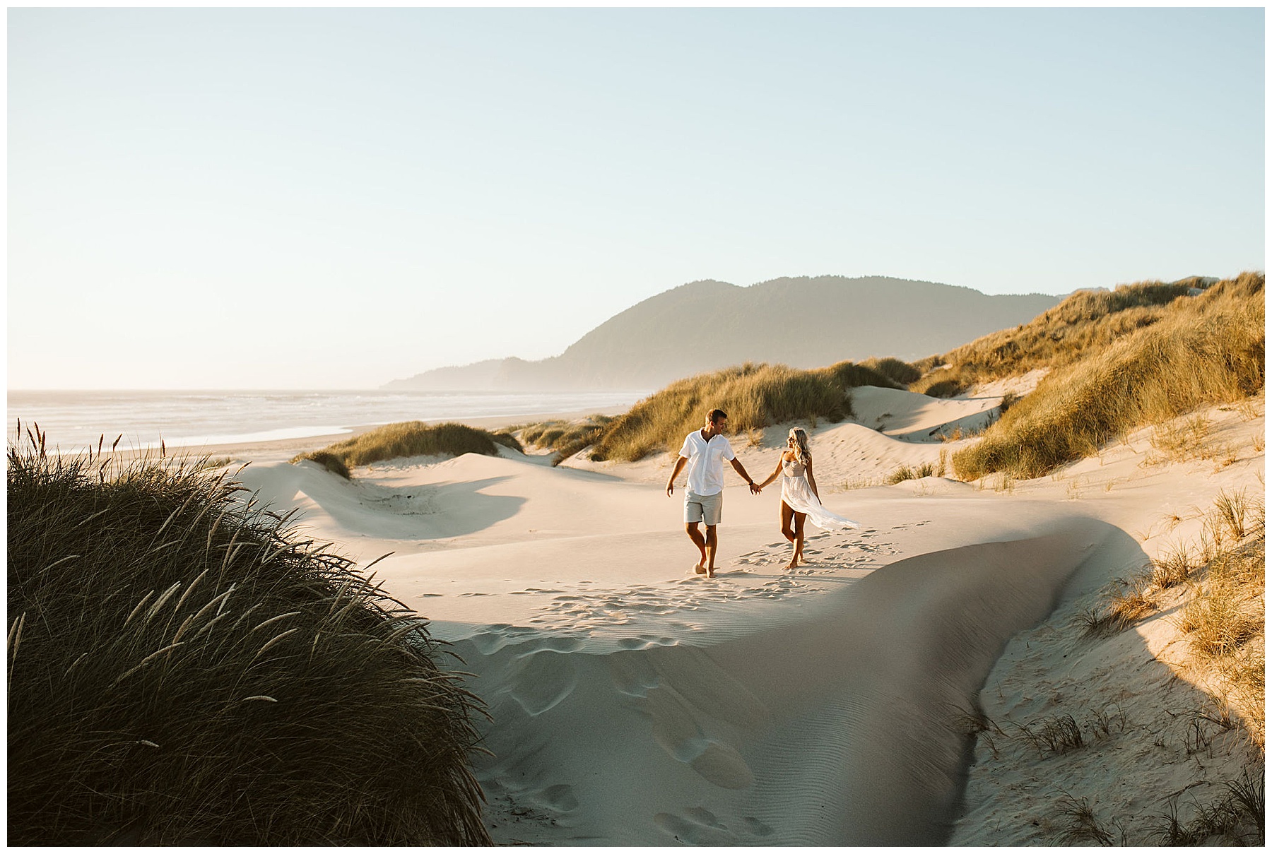 white male and white female holding hands on a beach with grassy hills in the background
