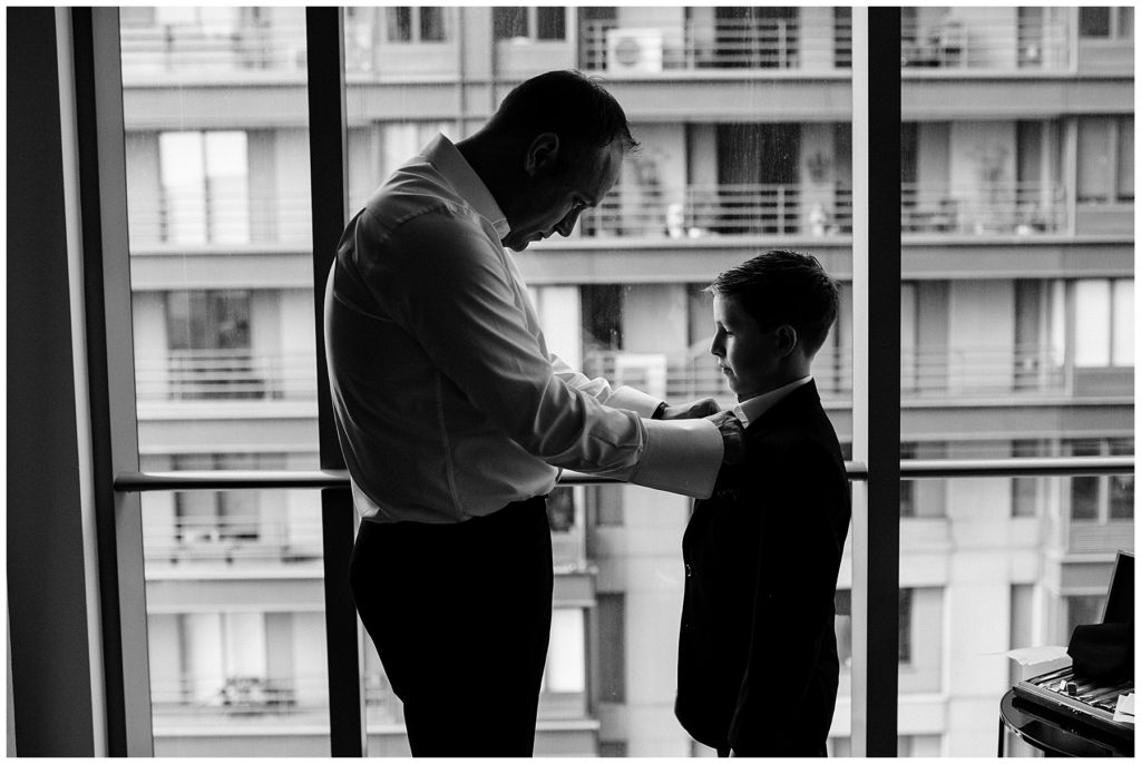 groom buttoning the ring bearer's shirt black and white photo