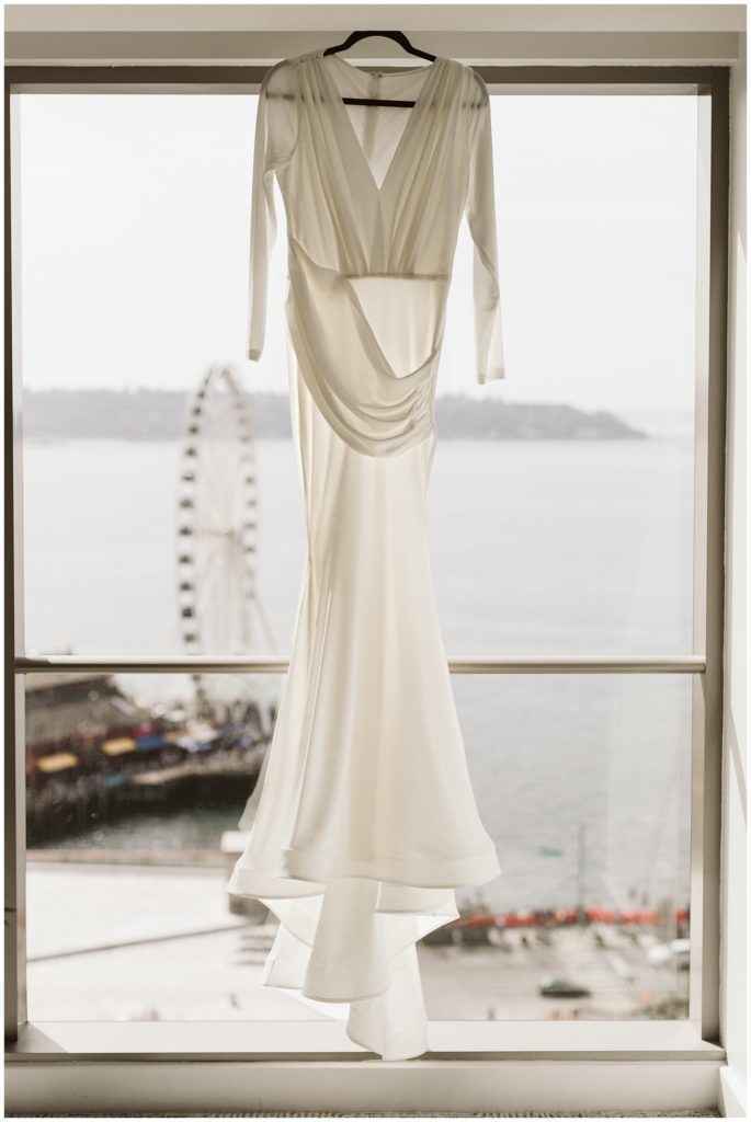 wedding dress hanging in front of window with water views and ferris wheel in the background