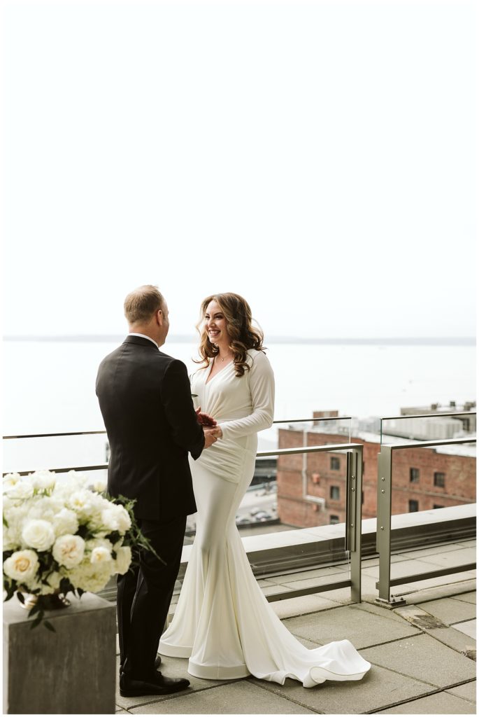 bride and groom holding hands on balcony with views in the background of the water and city