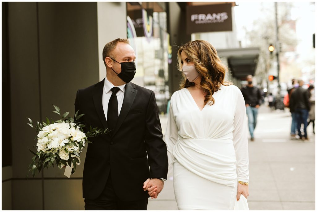 bride and groom walking in the city with masks on due to covid