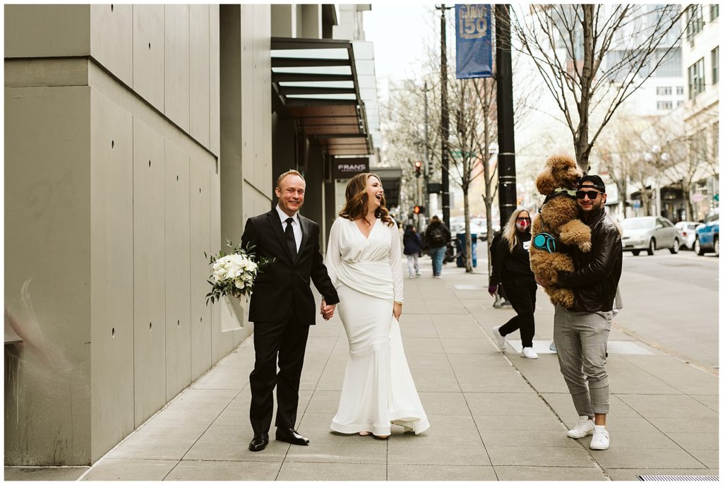 laughing bride and groom walking in downtown Seattle with a random guy holding a large fluffy brown poodle in his arms
