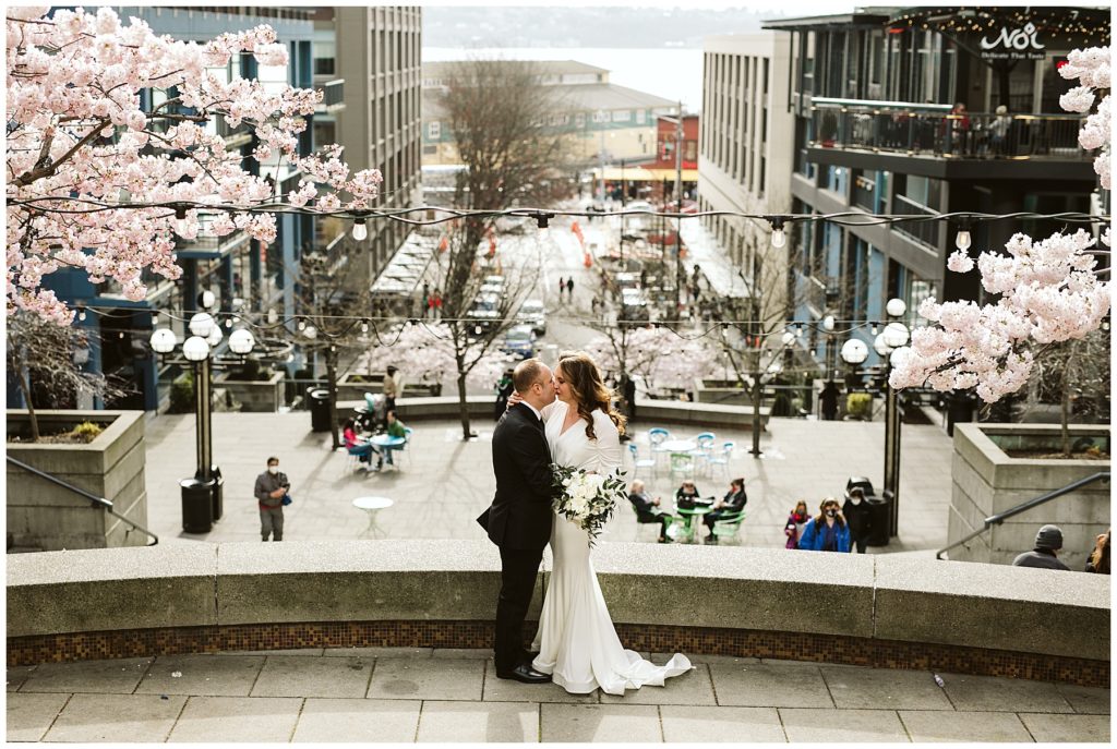 bride and groom kissing with the city in the background and cherry blossoms