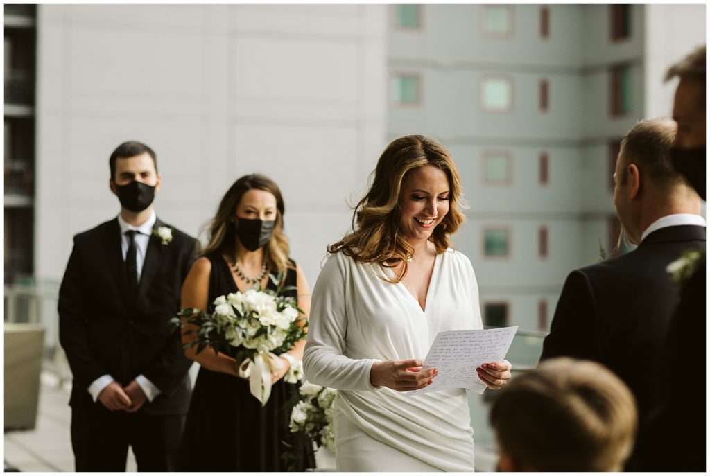 bride reading her vows with the wedding party behind her wearing medical masks because of covid