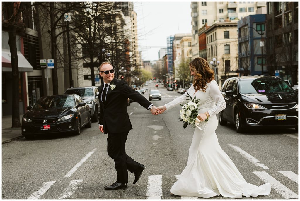 bride and groom walking across crosswalk holding hands and the groom is wearing sunglasses