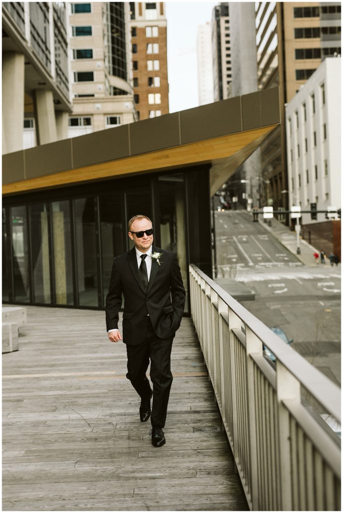 groom walking down stairs in a tuxedo with black sunglasses on 