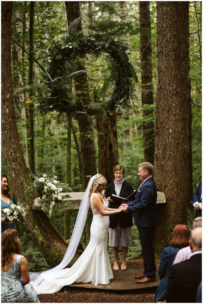 large fern wreath above bride and groom while officiant begins ceremony