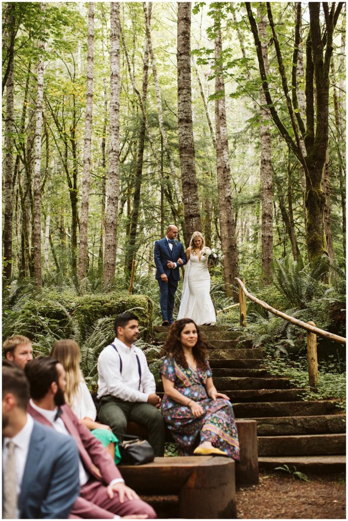 the bride and father of the bride walking down the isle in a outdoor forest ceremony