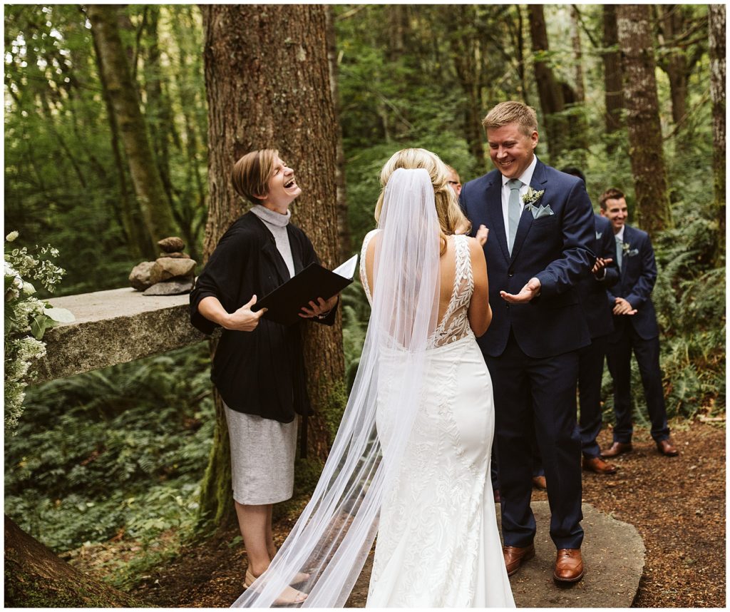 the officiant laughing with the bride and groom at the alter in a forest wedding venue