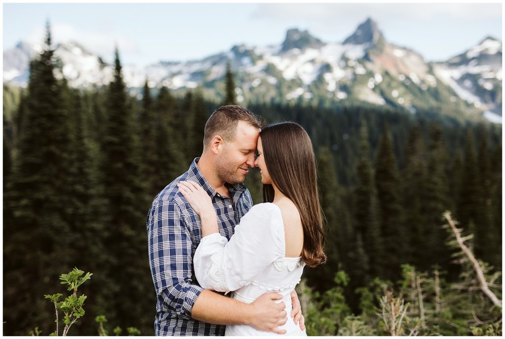beautiful couple holding each other in their arms and touching foreheads with the forest in the background shot by kelly lemon photography at mount rainier
