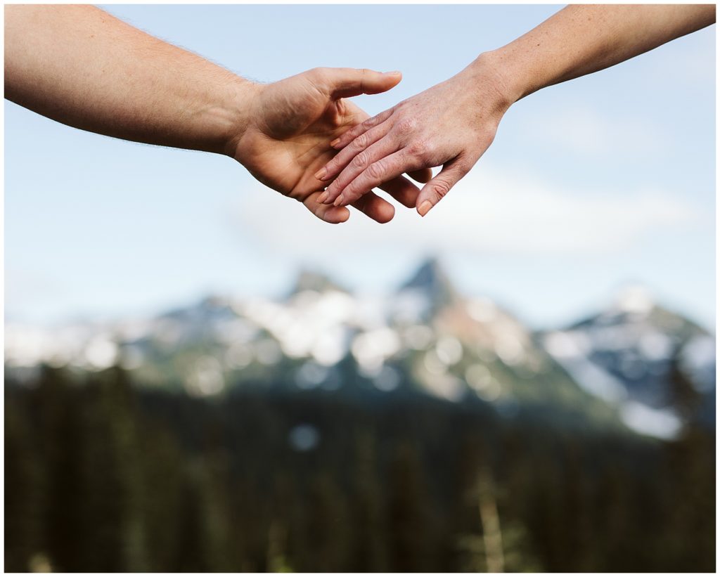 a close up of a couple holding hands with the mountains in the background