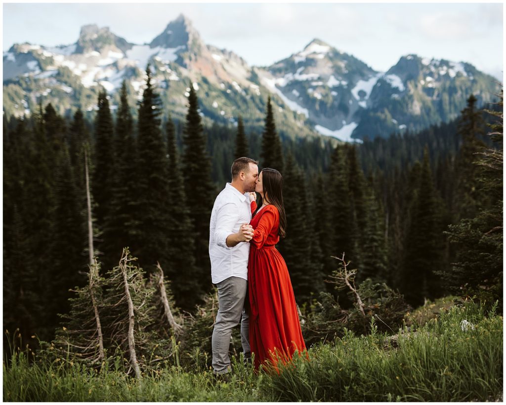 woman kissing her husband in a striking red dress with the mountains and forest behind them shot by kelly lemon photography 