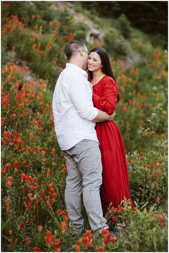 couple hugging while standing in grassy field with bright red flowers