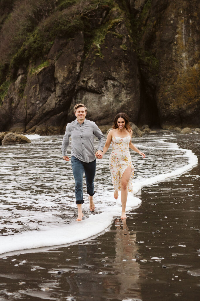 girl and boy walk through ocean during oceanside engagement shoot