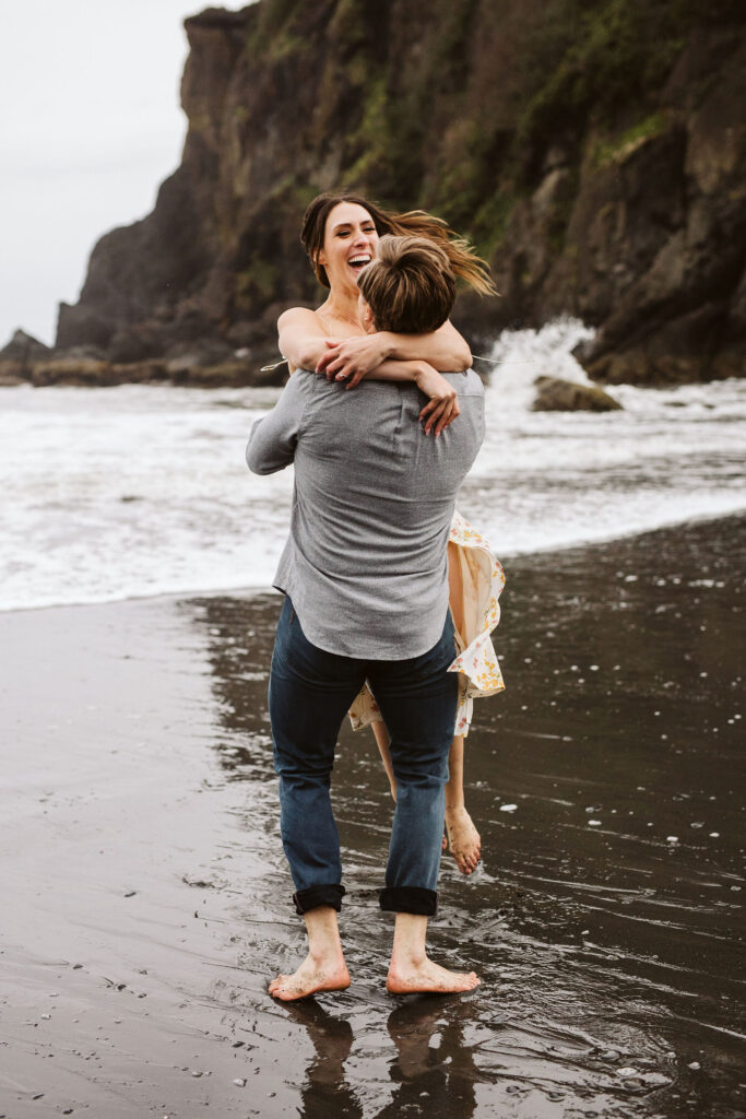 boy spins girl in ocean during engagement shoot