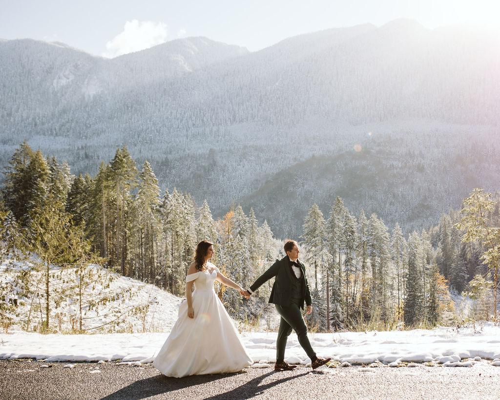 couple walks hand in hand down road with snowy backdrop