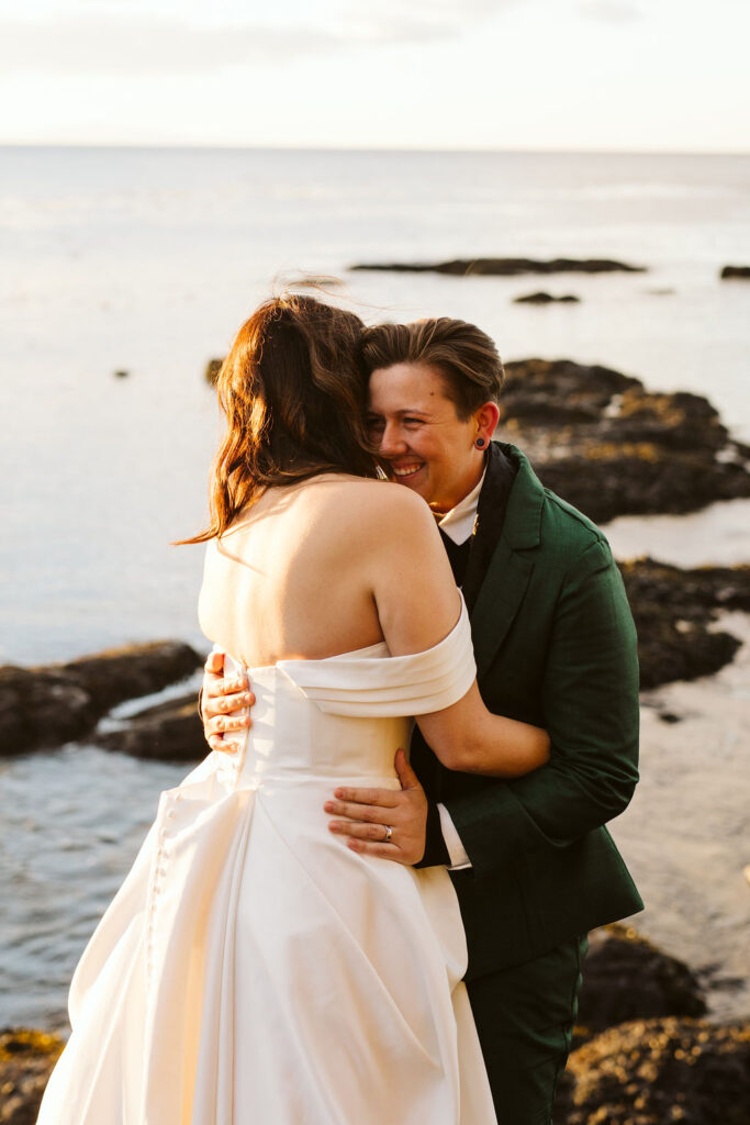 brides press foreheads against each other at sunset with ocean behind them