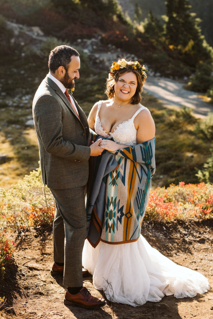 bride smiles while cuddle with groom wrapped in a blanket