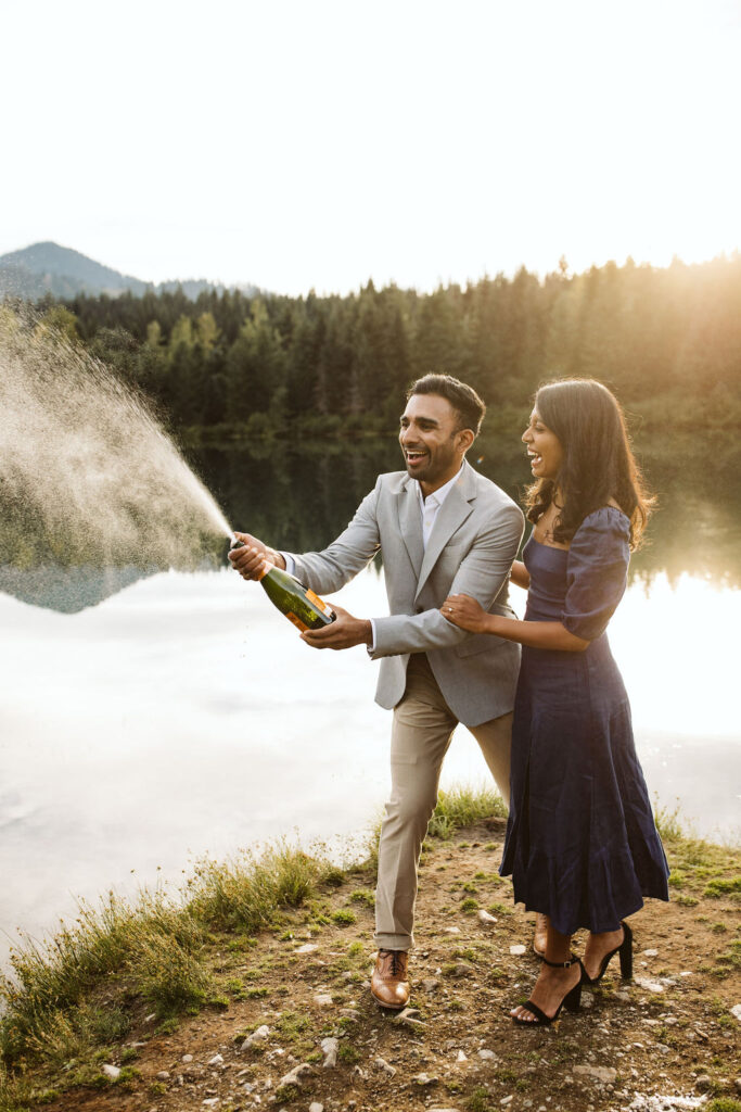 man and woman spray champagne during engagement shoot