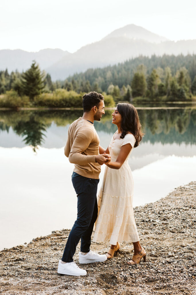 boy and girl stand in front of lake holding hands and smiling at each other