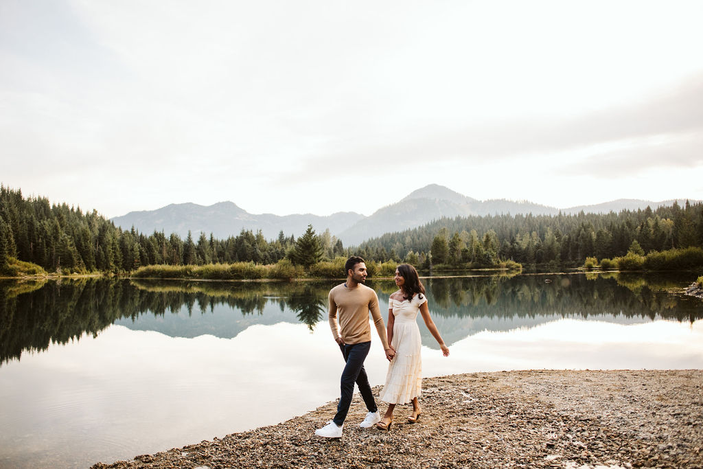 boy and girl walk in front of lake holding hands during gold creek pond engagement session