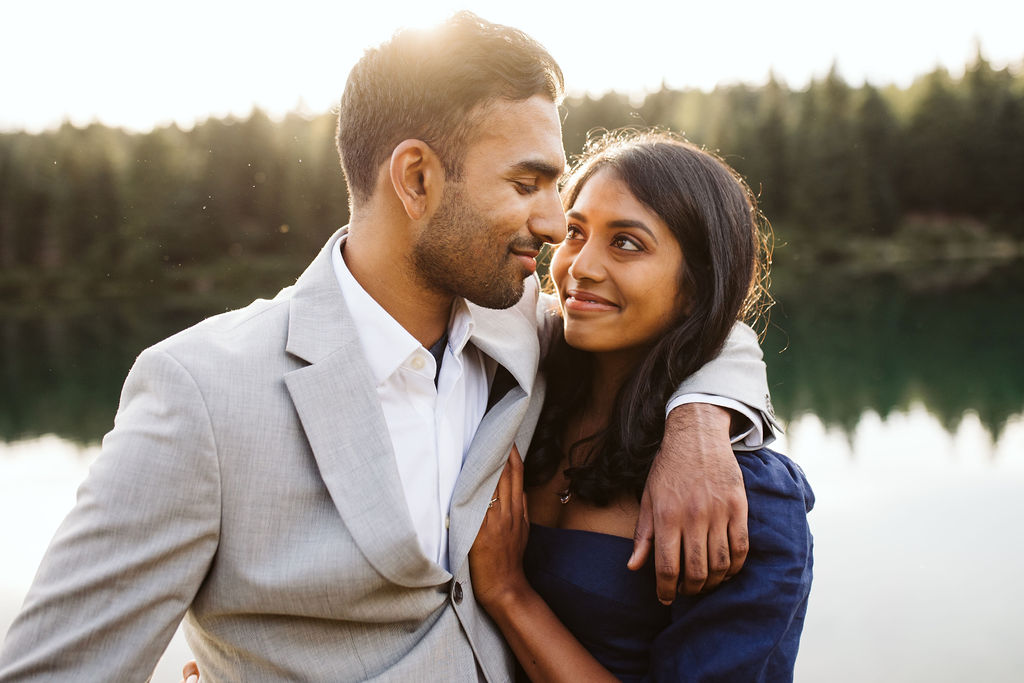 man in grey suit has an arm around womans shoulders in front of a lake