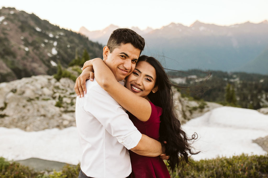 boy and girl hug while smiling with mountains behind them